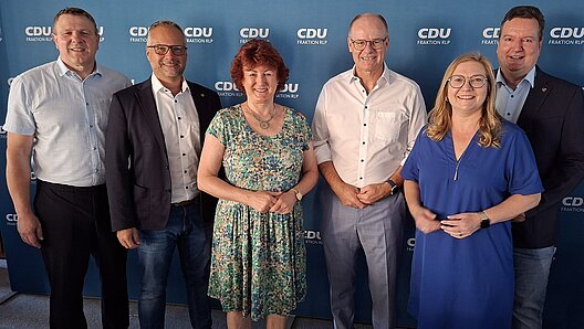 Gruppenbild mit vier Männern udn zwei Frauen vor einer dunkelblauen Logo-Wand