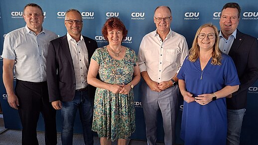 Gruppenbild mit vier Männern udn zwei Frauen vor einer dunkelblauen Logo-Wand