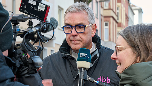 Mann vor Kamera mit Redakteurin