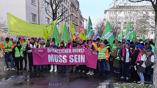 Transparent "Öffentlicher Dienst muss sein!", gehalten von einer gemischten Gewerkschaftsgruppe an der Spitze einer Menschenmenge