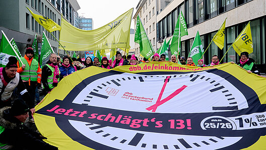 Menschengruppe hält an der Spitze eines Demonstrationszuges ein Rundbanner mit Uhren-Logo