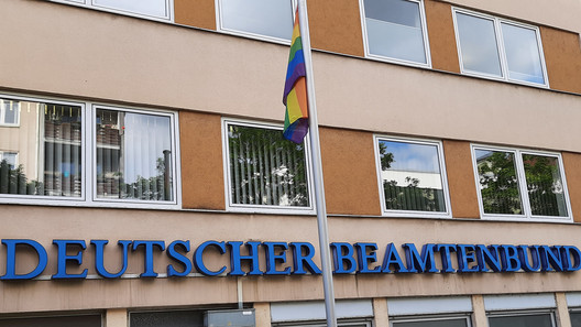 Regenbogenfahne am Fahnenmast vor Bürogebäudefassade dbb Haus 