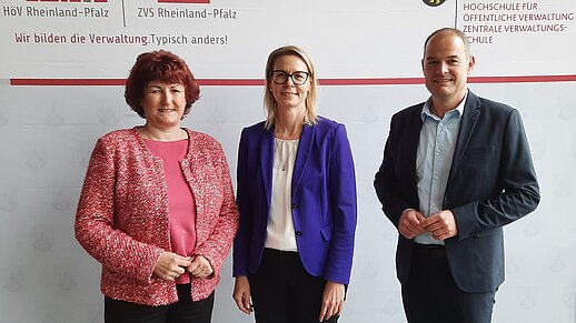 Drei Personen vor eine Logo-Wand.