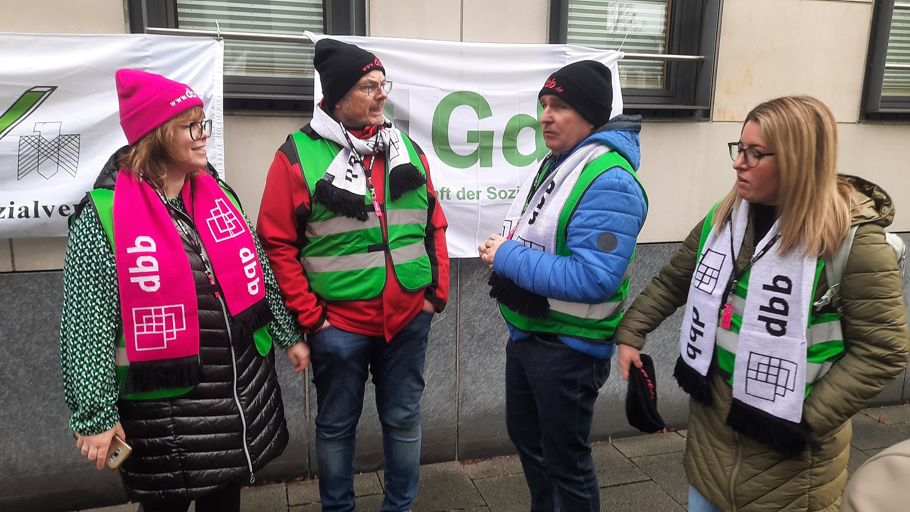 Zwei Frauen udn zwei Männer in Gewerkschaftsdress vor Banner.